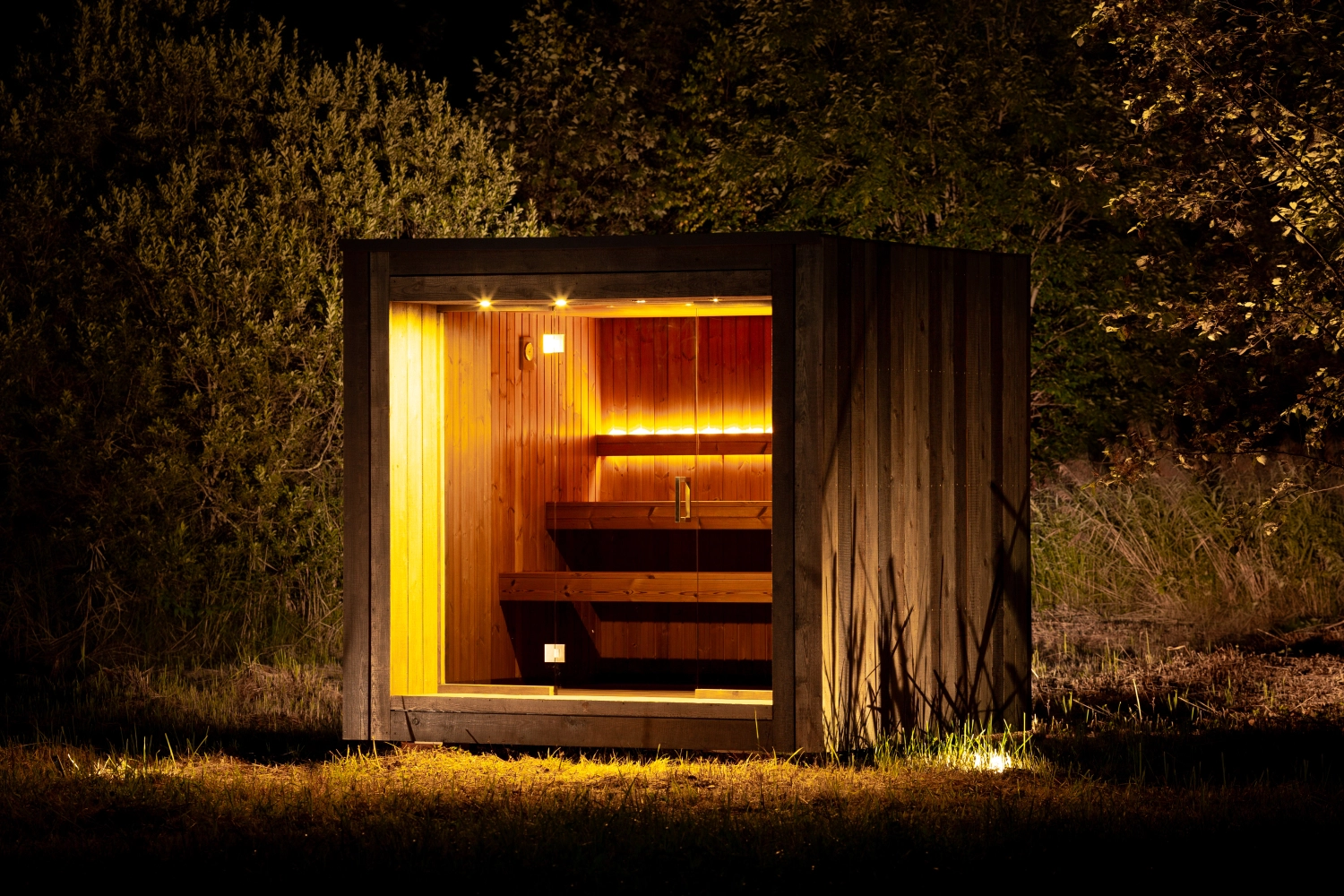 Maja Sanctuary cube sauna glowing warm at night in dark woodland
